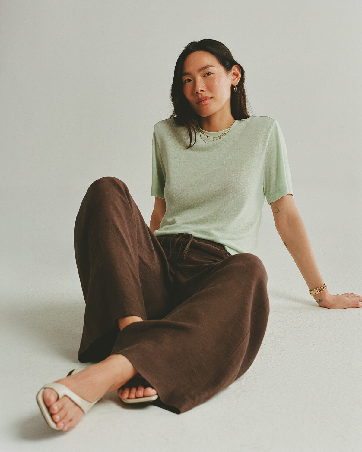 Woman sitting on the floor wearing a light green t-shirt and brown pants against a plain background