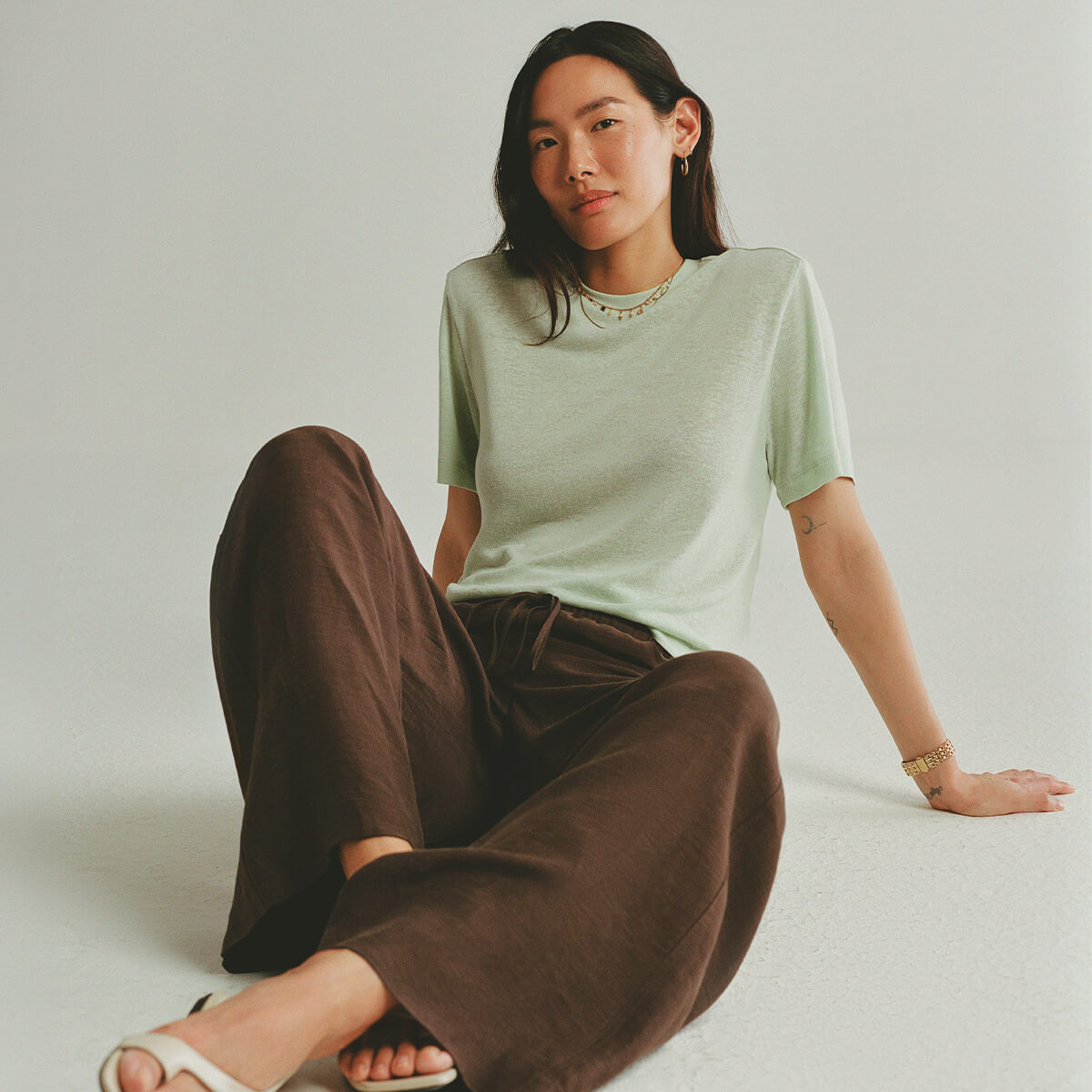 Person wearing a light green t-shirt and brown pants sitting on a plain background