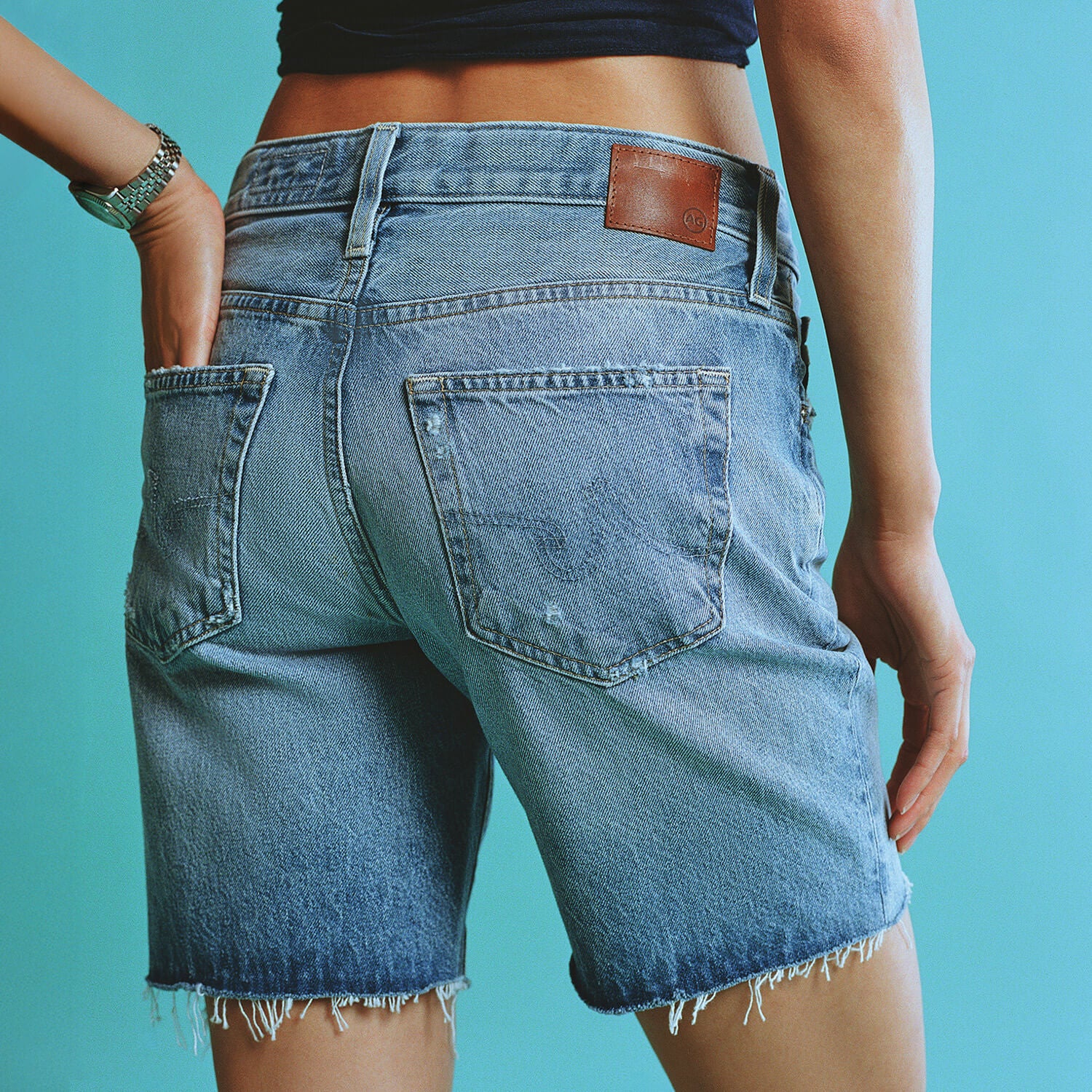 Person wearing blue denim shorts against a teal background