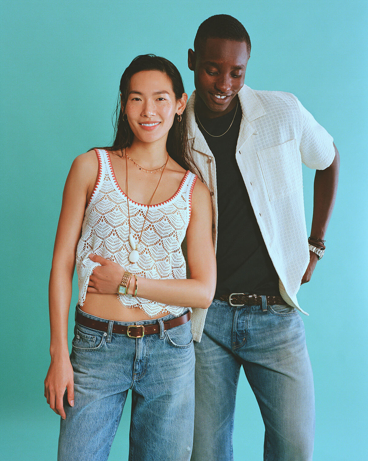 Two people standing close together against a teal background