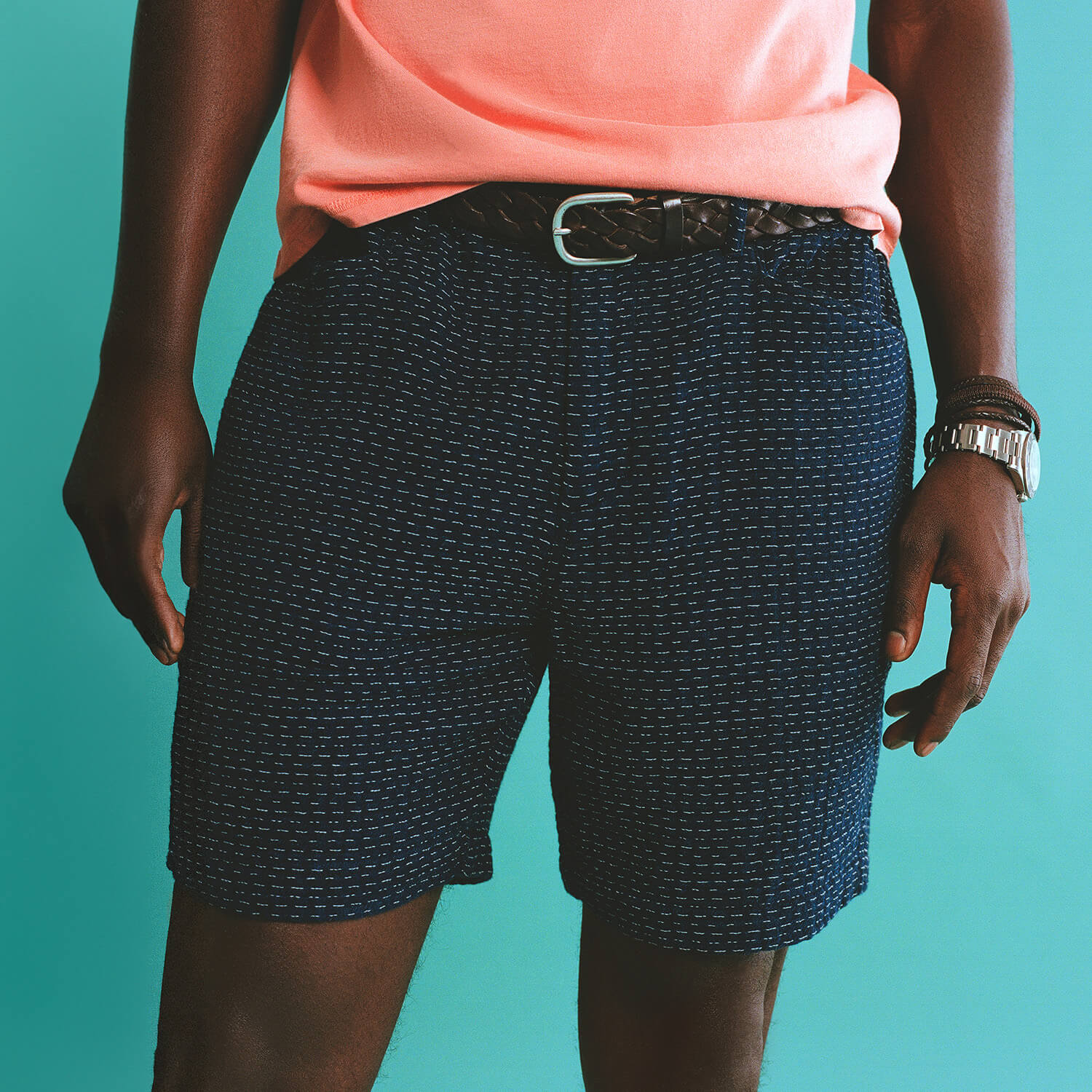 Person wearing navy patterned shorts and a pink top on a teal background