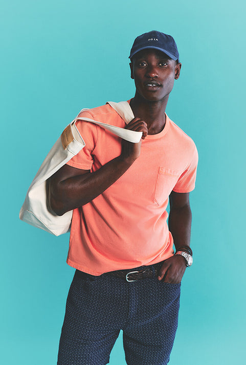 Man wearing a peach t-shirt, navy cap, and navy shorts against a teal background