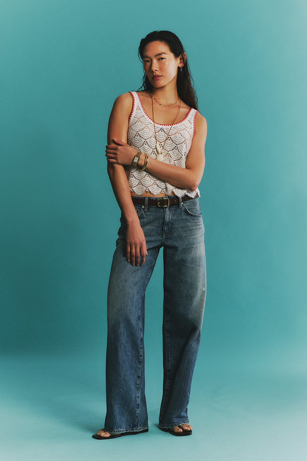 Woman wearing a white sleeveless top and blue jeans against a teal background