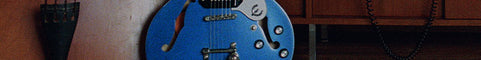 A blue electric guitar with gold hardware, shown in a close-up indoor shot against a wooden background.
