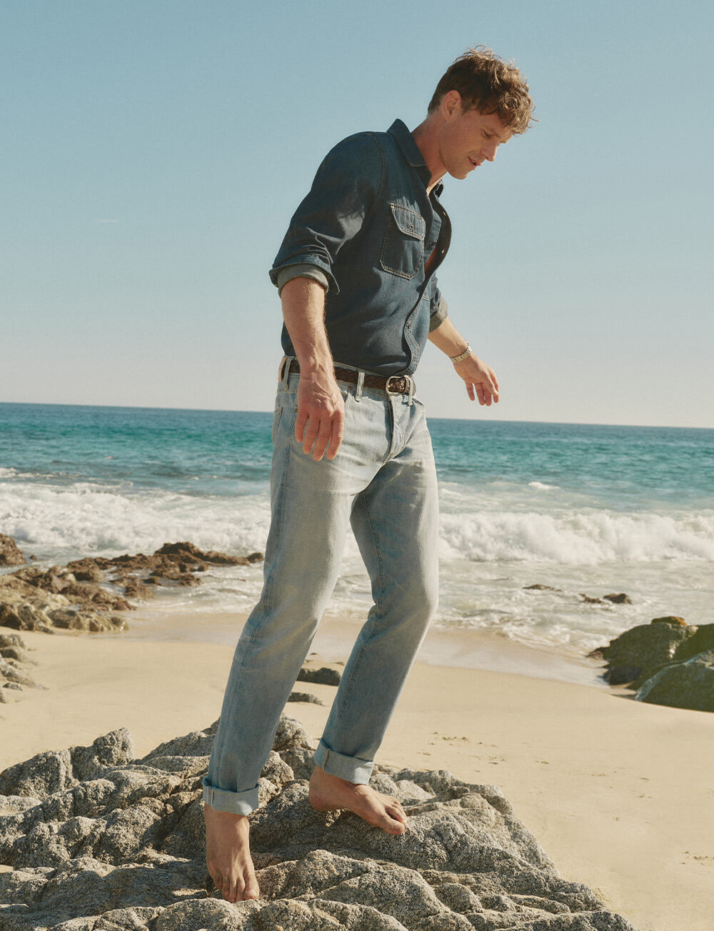 Man in blue shirt and blue jeans in front of beach