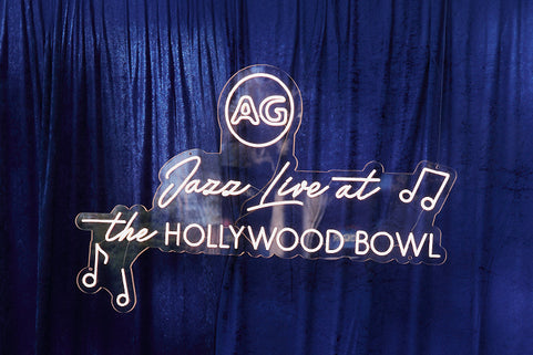 A blue curtain backdrop with a glowing white neon-style sign that reads 'Jazz Live at the Hollywood Bowl' and includes an 'AG' monogram logo.