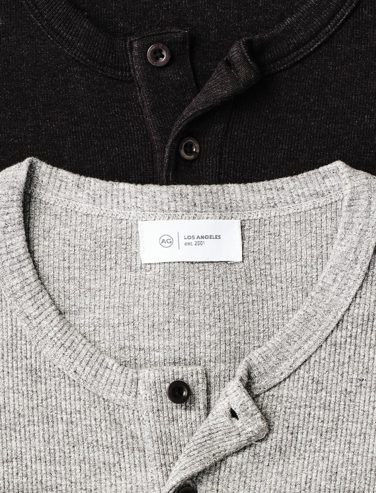 Close-up of a light gray ribbed henley sweater, layered over a black ribbed henley sweater.