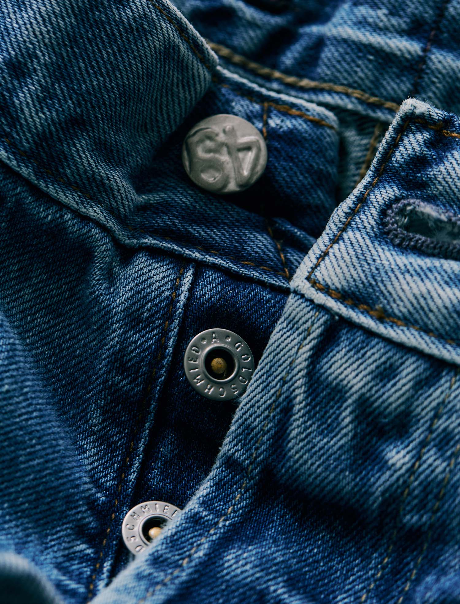 Close-up of a blue denim garment showing the button placket, with metal buttons and visible St. Louis denim branding.