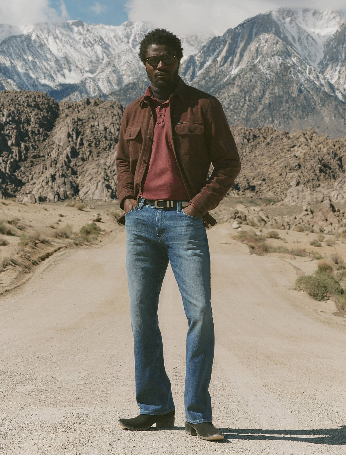 Man standing on a dirt road with mountains in the background