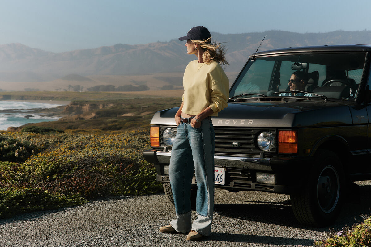 Person standing next to a vintage SUV by a scenic coastal road