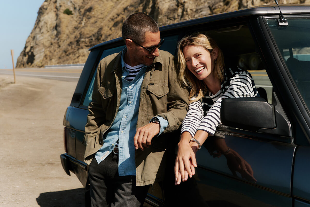 Man and woman sitting in a convertible car with a scenic background