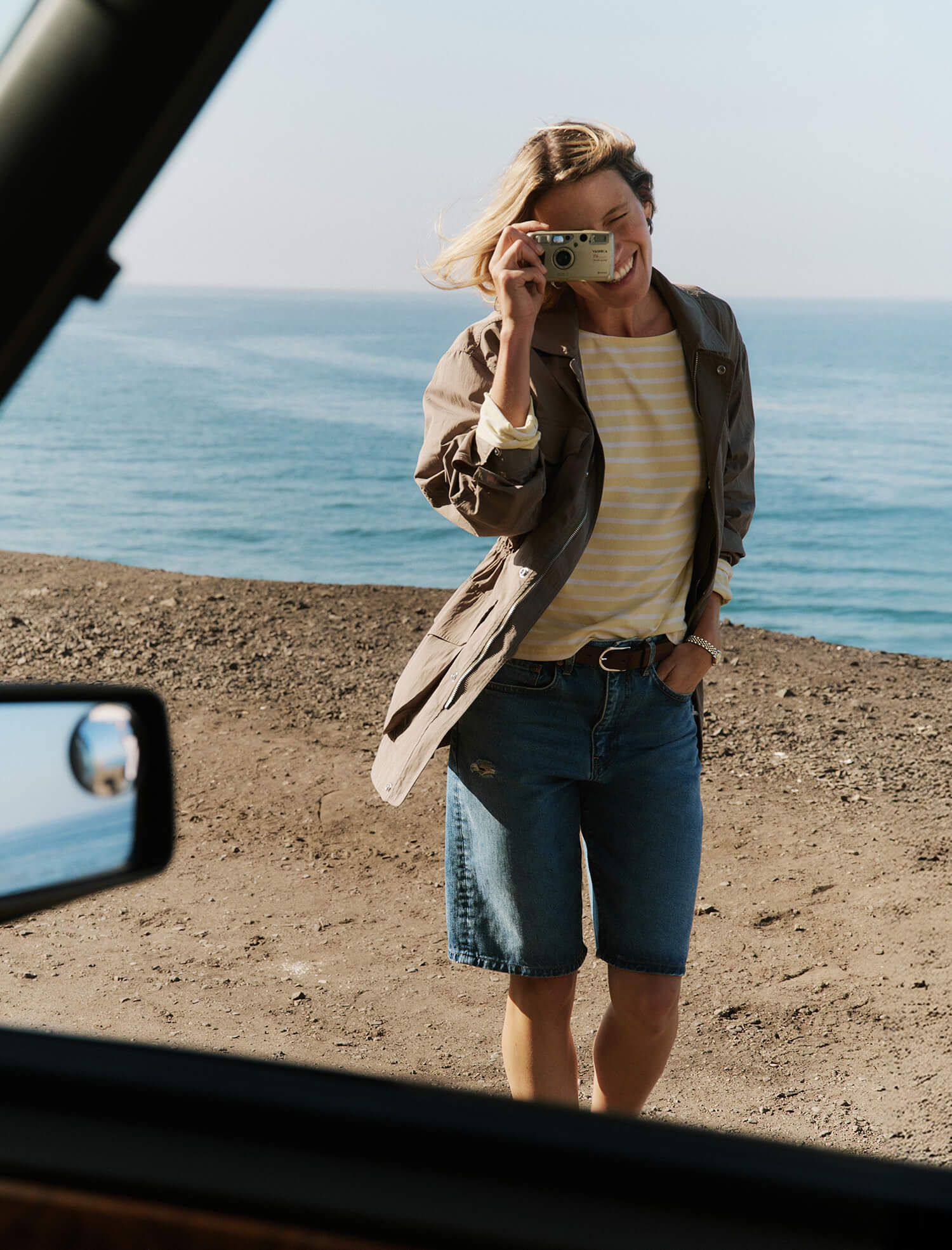 Person taking a mirror selfie by the ocean with a car's interior visible.