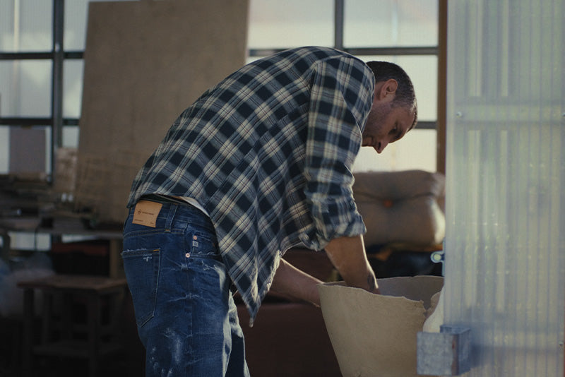 Man unpacking a box in a room with furniture and large windows.
