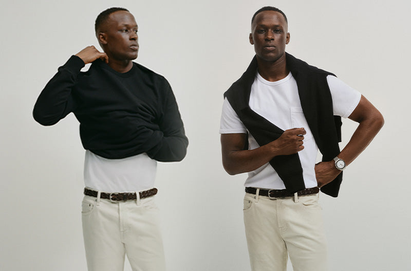 Two men wearing black vests over white shirts with beige pants on a plain background