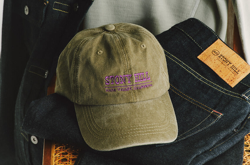 Olive green cap with 'Stony Hill' logo on a folded denim jacket.