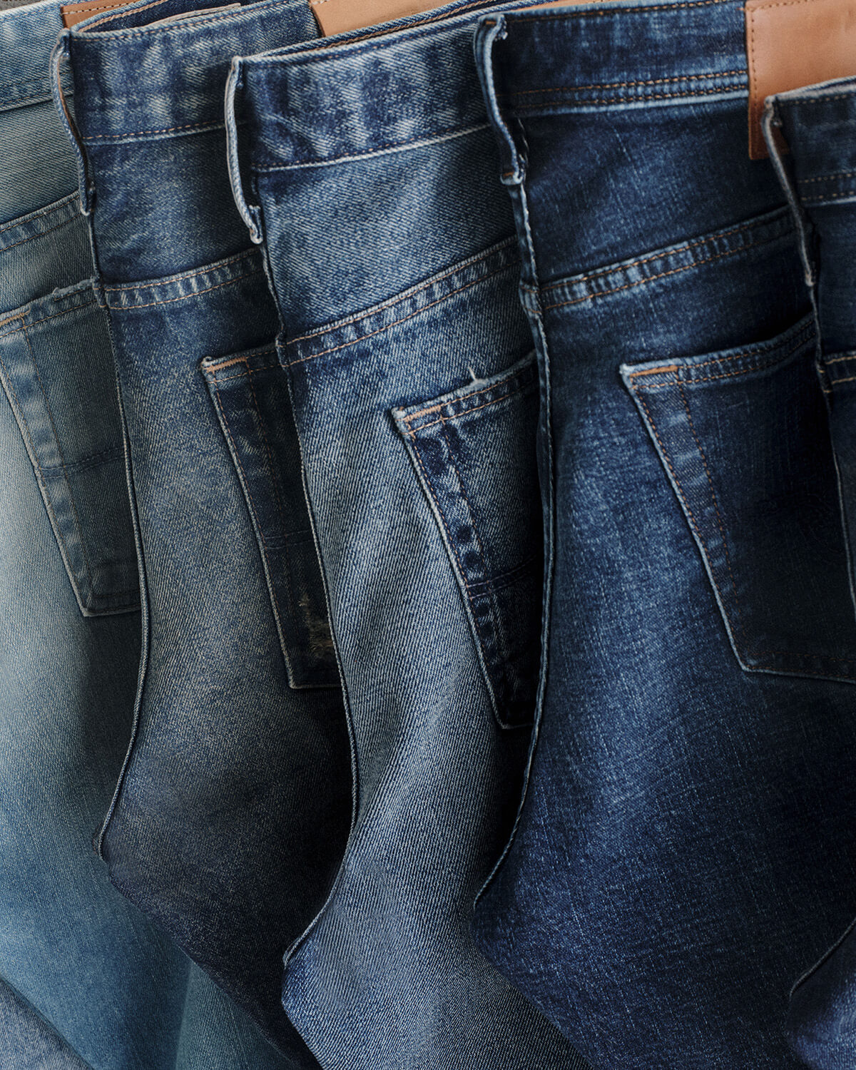 Close-up of several blue denim jeans hanging side by side, showing the back pockets and dark wash fabric texture.
