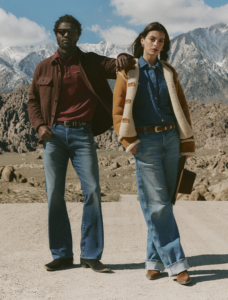 Two people standing in a desert landscape with mountains in the background