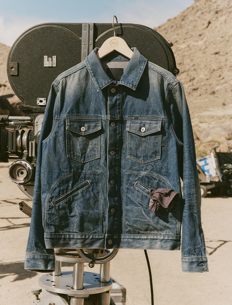 Denim jacket on a hanger against a desert backdrop with vintage equipment.