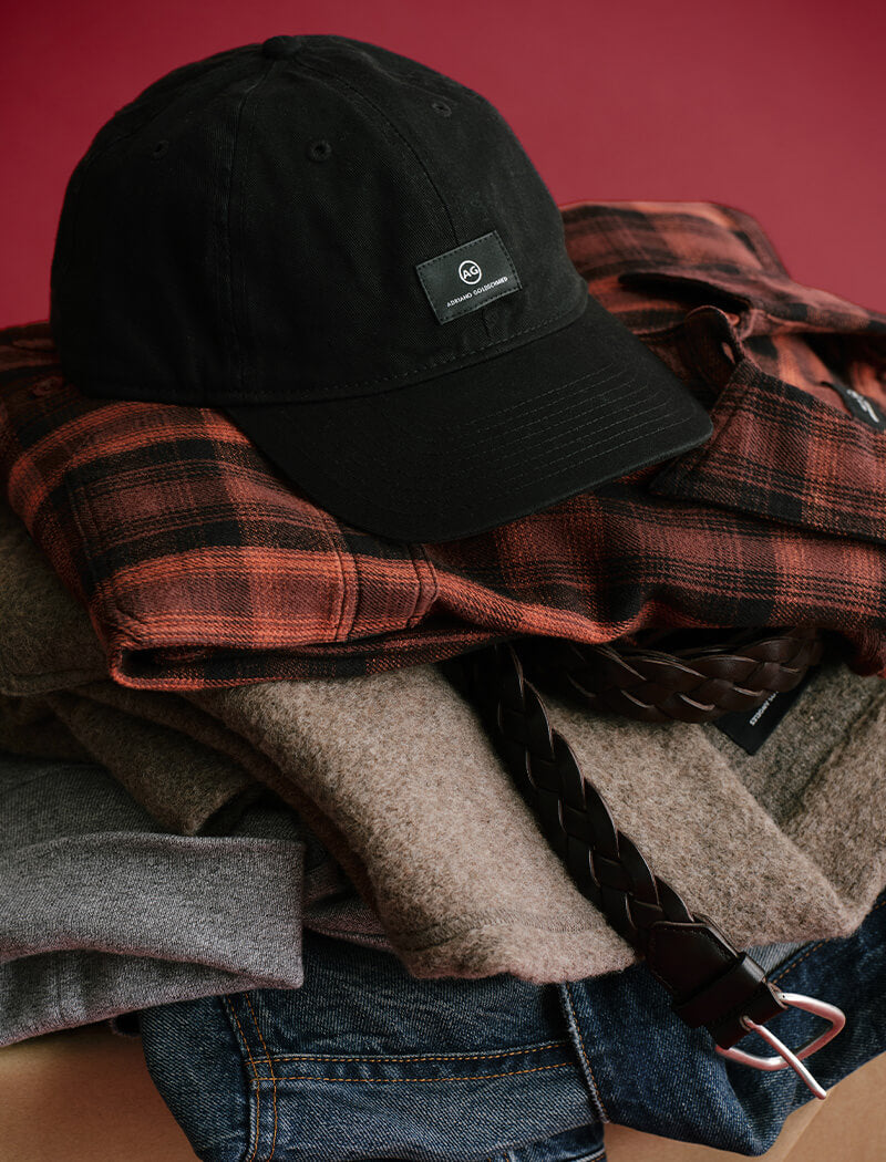 Black cap on a stack of plaid shirts with a red background