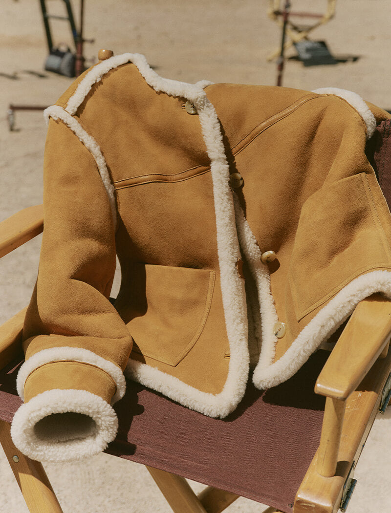 Brown shearling jacket on a chair with a blurred outdoor background