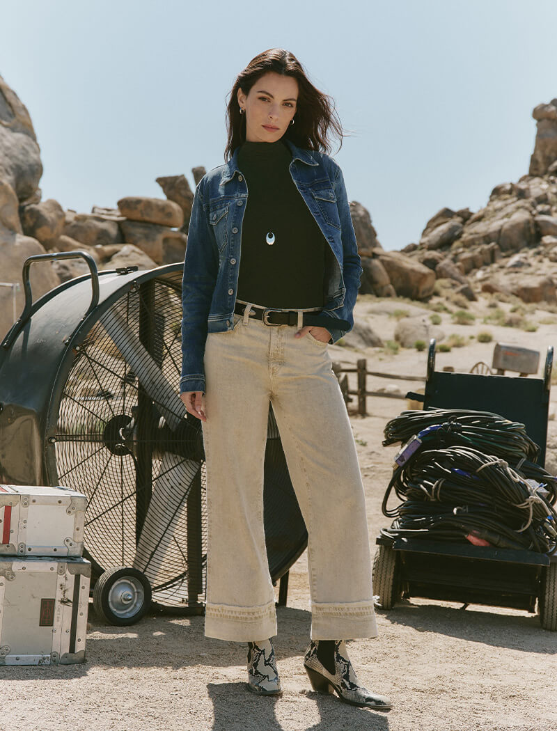 Woman standing in a desert-like setting with rocky formations and equipment.