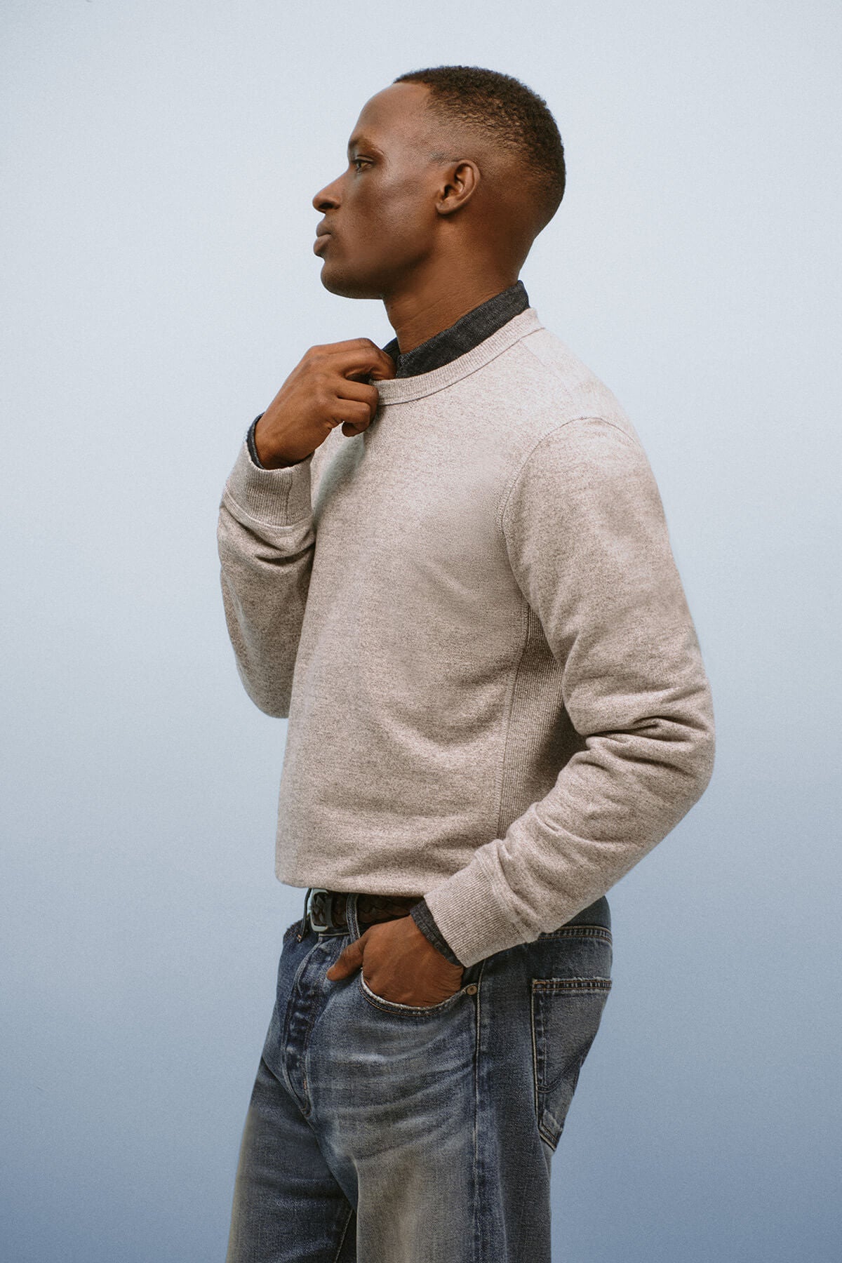 Man wearing a beige sweater and blue jeans against a light gray background