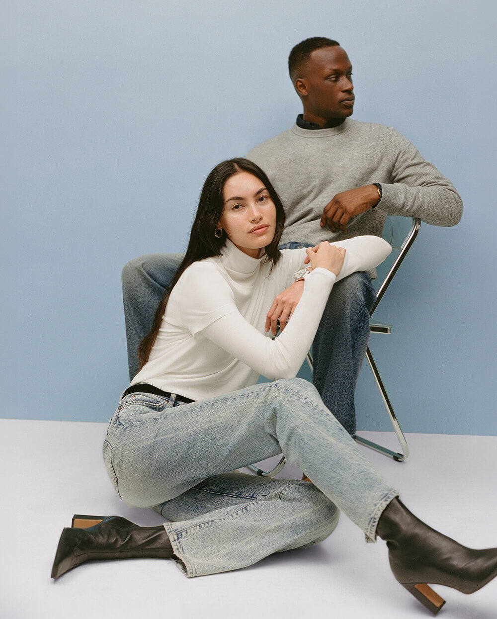 Two people sitting on a white surface with a light blue background