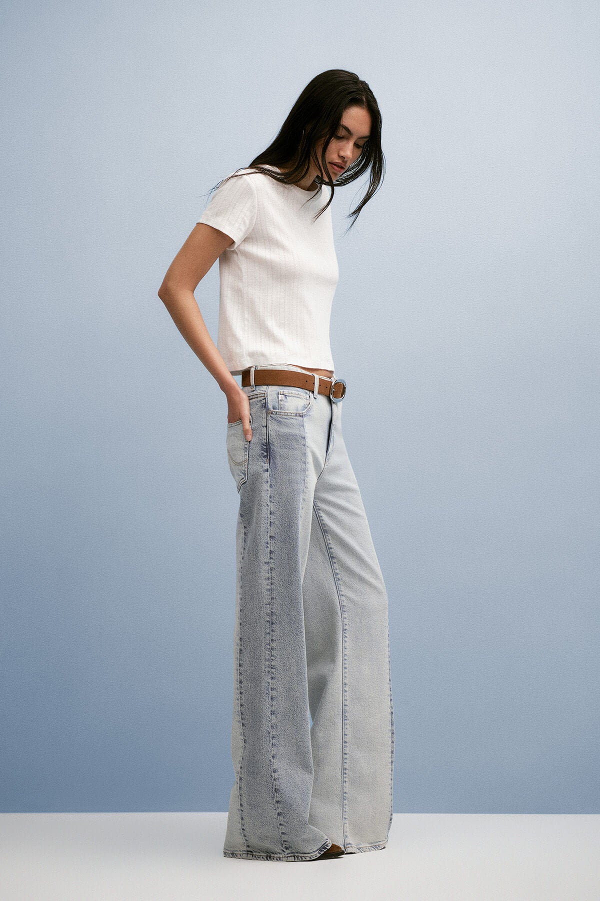 Woman wearing a white top and light blue jeans against a plain background