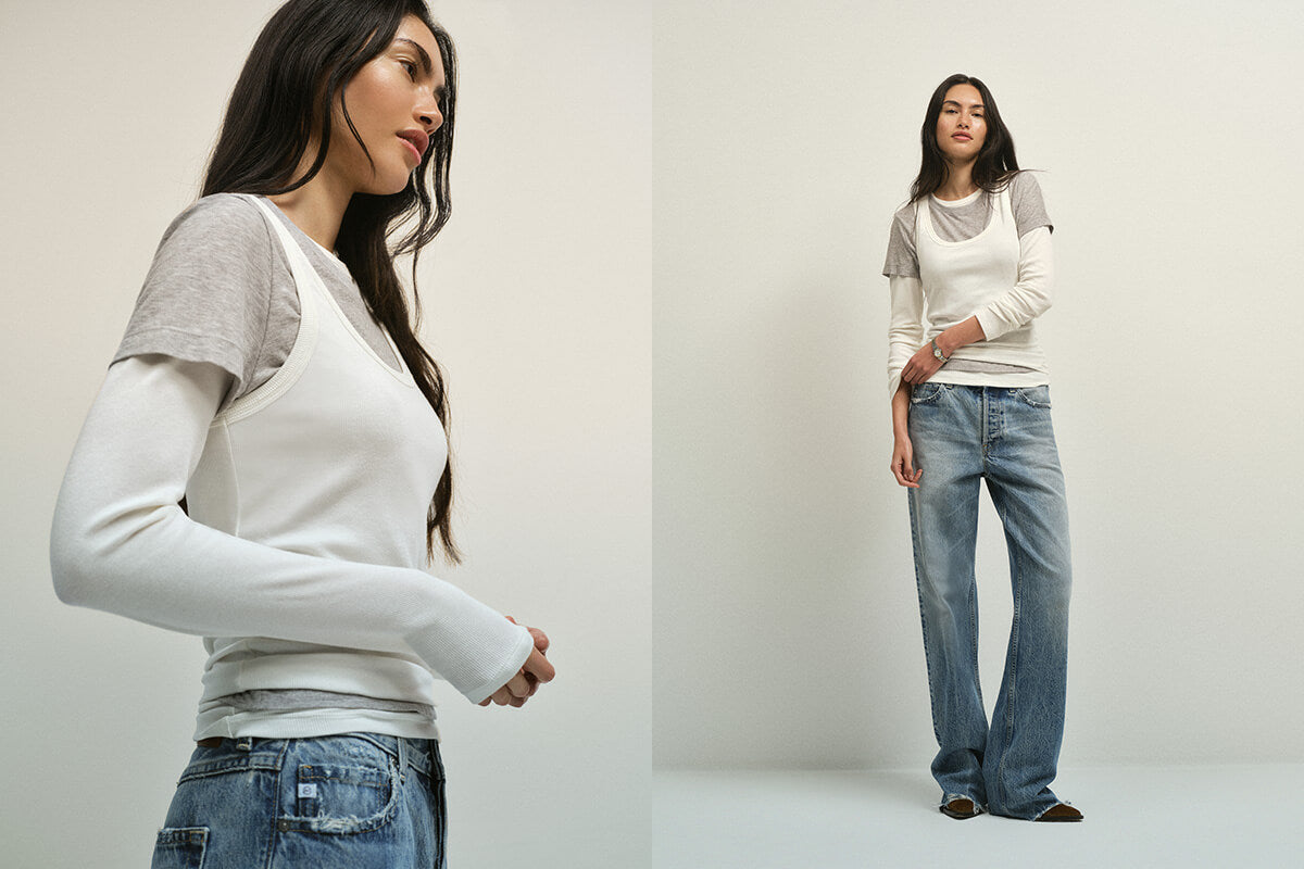 Two women wearing matching outfits of white tops and blue jeans against a plain background.